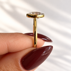 Side detail of an oval cut diamond in a yellow gold bezel setting on a slim polished band