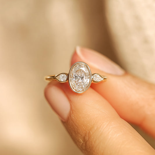 Bezel Set Oval Cut Moissanite Ring With Pear Side Stones And Diamond-Like Sparkle In Yellow Gold Setting