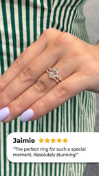 Hand with lavender nails wearing a rose gold oval diamond engagement ring stacked with a matching wedding band of marquise and round diamonds, shown against a green and white striped apron, with a five-star customer review from Jaimie overlaid at the bottom