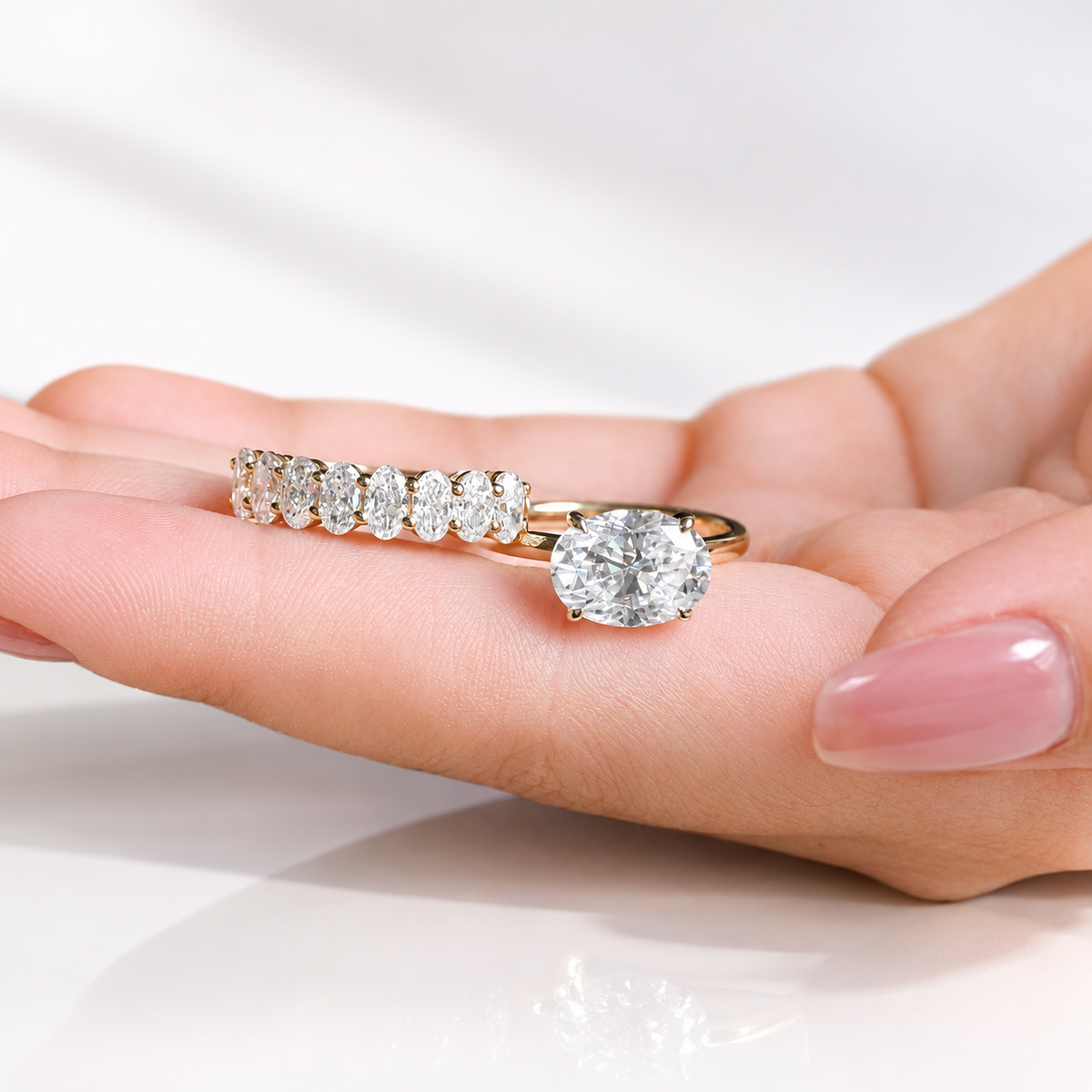 Angled view of an east west oval cut colorless ring stone with brilliant facets and four prongs
