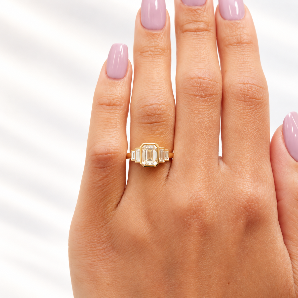 Emerald cut diamond center stone in a yellow gold bezel setting, flanked by two graduated baguette side stones on each side