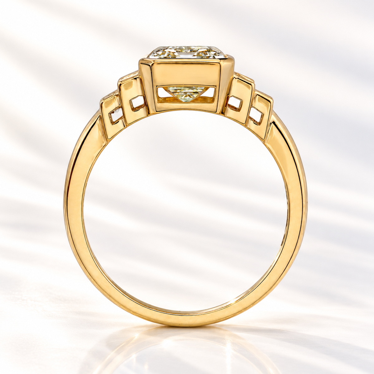 Side profile of an emerald cut diamond in a yellow gold bezel setting with stepped baguette side stones and an open gallery