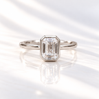Emerald cut diamond center stone in a white gold bezel setting on a slim polished band