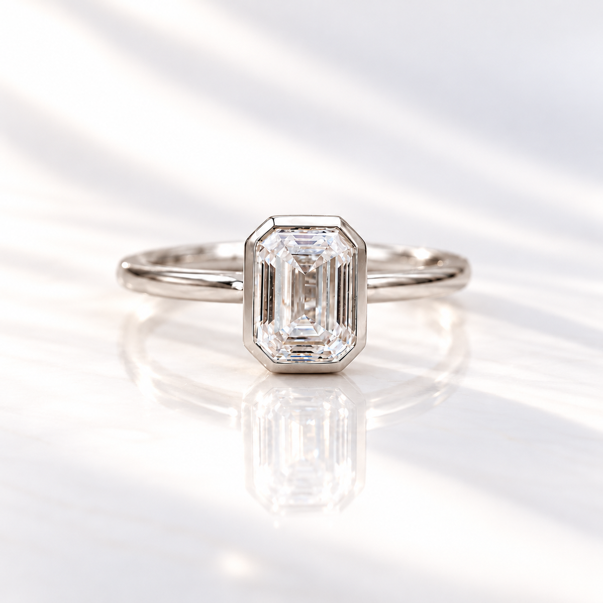 Emerald cut diamond center stone in a white gold bezel setting on a slim polished band