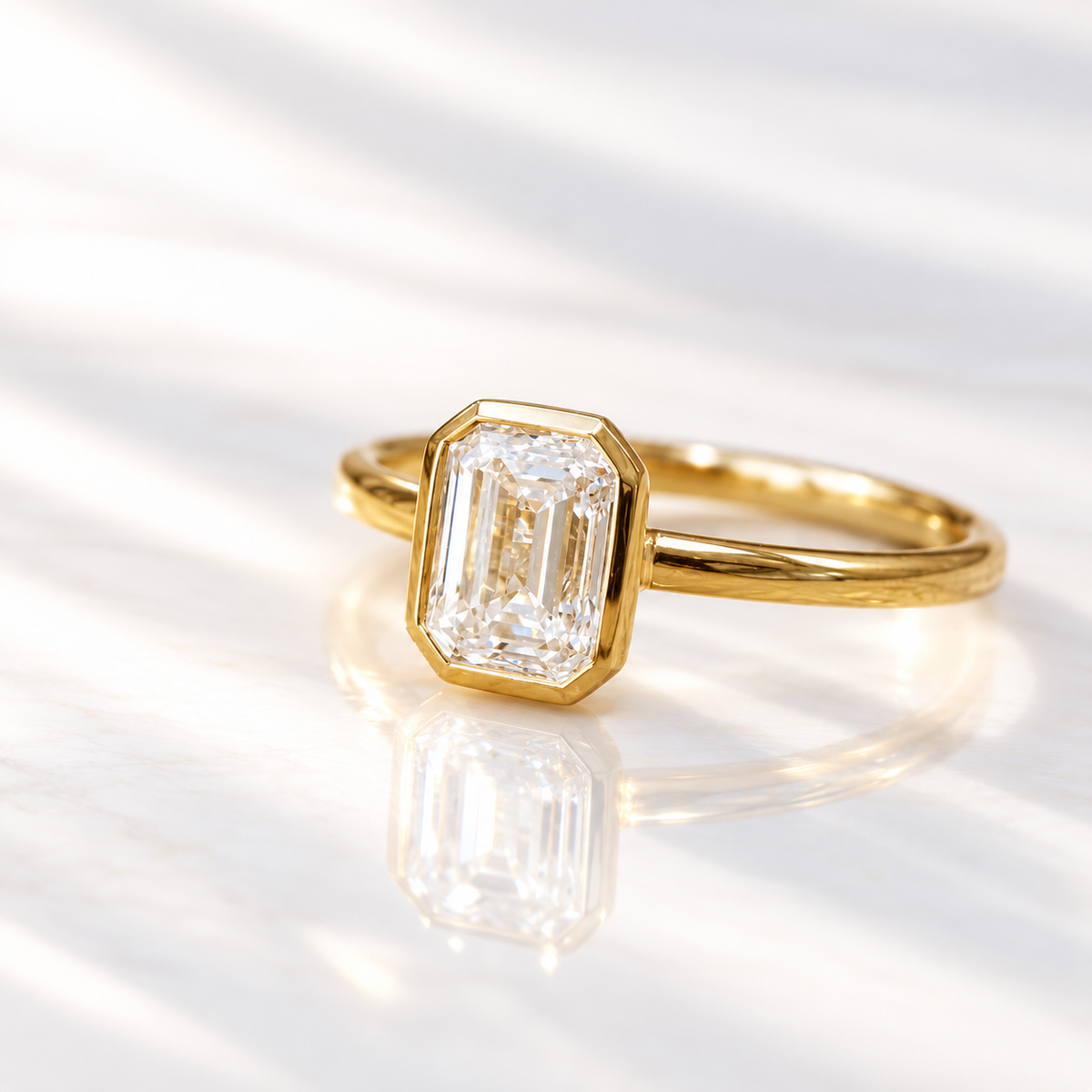 Angled view of an emerald cut diamond center stone in a yellow gold bezel setting on a slim polished band