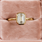 Top view of an emerald cut diamond center stone in a yellow gold bezel setting on a slim polished band