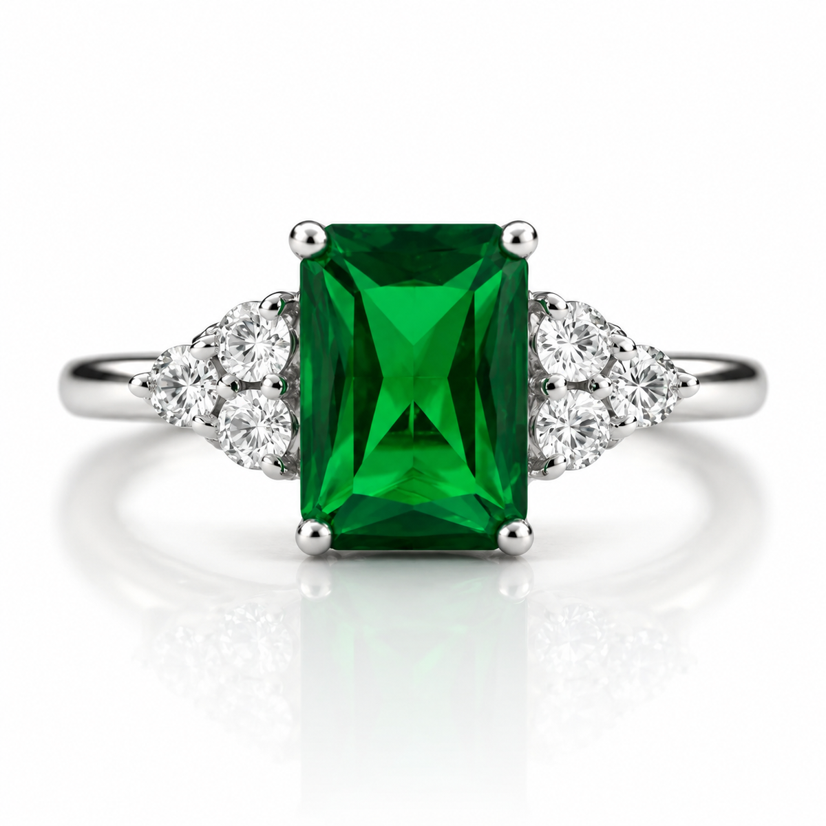 An emerald-cut green gemstone ring set in a silver-colored metal band with small clear accent stones on either side, shown on a clean white background with a soft reflection.