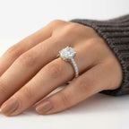 Four-prong oval cut diamond engagement ring set in white gold or platinum with a delicate hidden halo and pavé diamond band, worn on a hand.
