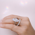 Hand wearing a diamond ring with a marquise-shaped center stone and a matching band on a light background