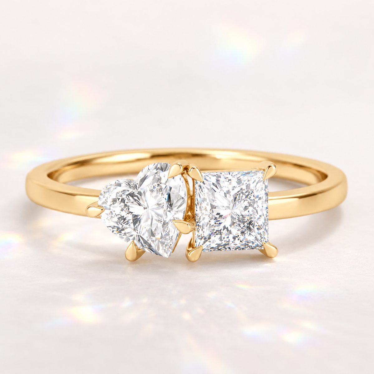 18K gold three-stone engagement ring featuring a heart-shaped diamond paired with a square princess-cut diamond, set in polished gold with delicate prongs on a white background.