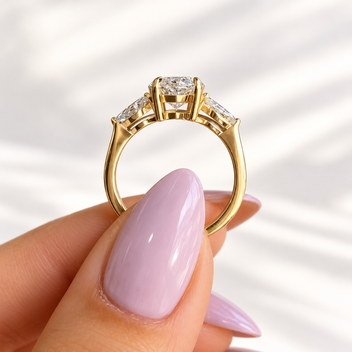 Side profile of a yellow gold three stone ring with a marquise cut center diamond held by prongs and tapered marquise side stones