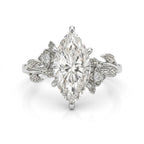 A silver-toned diamond ring featuring a marquise-cut center diamond flanked by small round diamonds and leaf-like floral details on the band, shown on a clean white background.