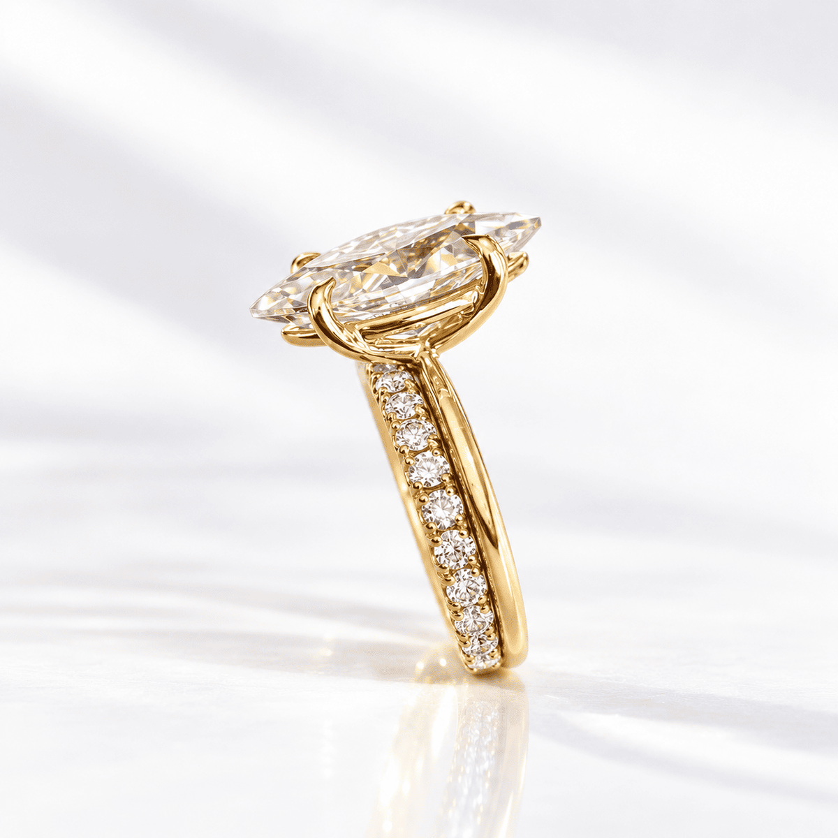 Side profile of a marquise diamond engagement ring with a pavé diamond band, set in yellow gold on a bright white surface.
