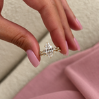Fingers with pink manicured nails holding a yellow gold marquise diamond engagement ring and matching wedding band with bezel-set marquise and round diamonds, with a pink fabric background
