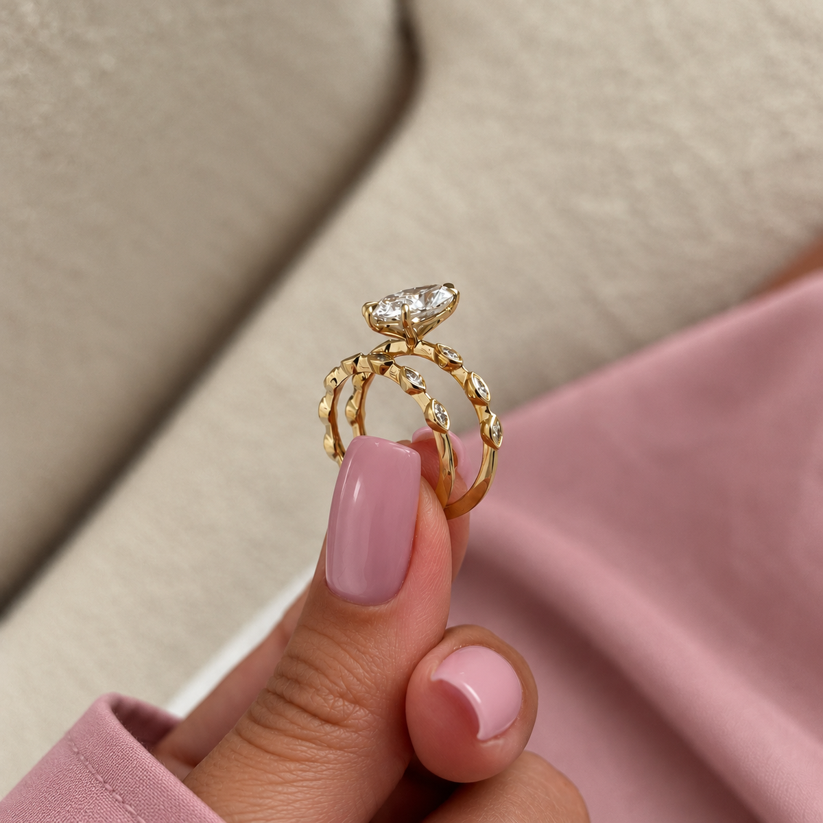 Fingers with pink nails holding a yellow gold marquise diamond ring and a stacked wedding band upright, showing the bezel-set marquise diamonds along both bands
