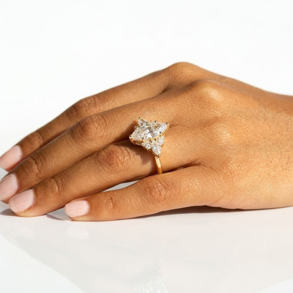 Marquise cut moissanite engagement ring set in yellow gold with an asymmetric cluster of round and pear side diamonds, worn on the hand.