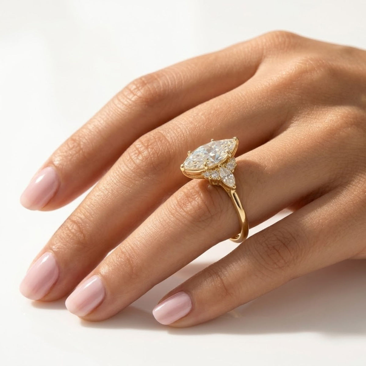 Marquise cut moissanite engagement ring set in yellow gold, featuring cluster diamond accents on the basket and shoulder, worn on a hand.