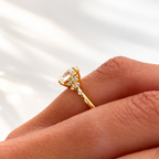 Close-up side view of a hand wearing a yellow gold oval diamond engagement ring with small cluster diamonds along the band