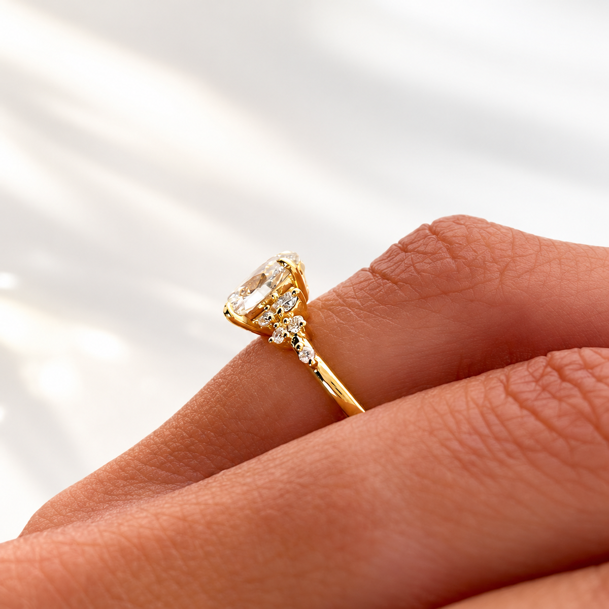 Close-up side view of a hand wearing a yellow gold oval diamond engagement ring with small cluster diamonds along the band