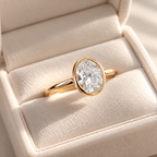Angled view of an oval cut diamond center stone in a yellow gold bezel setting on a slim polished band