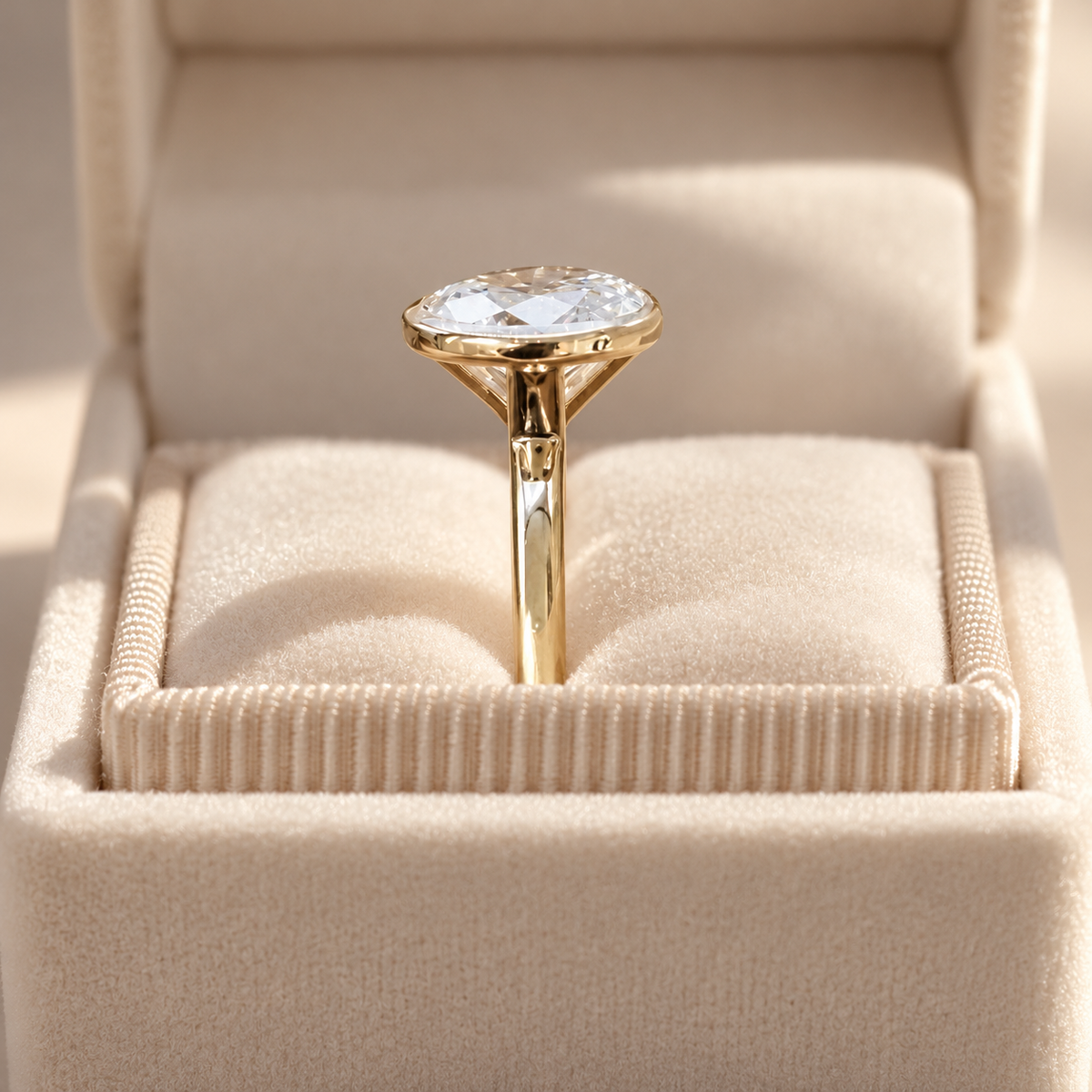 Side profile of an oval cut diamond in a yellow gold bezel setting on a slim polished band