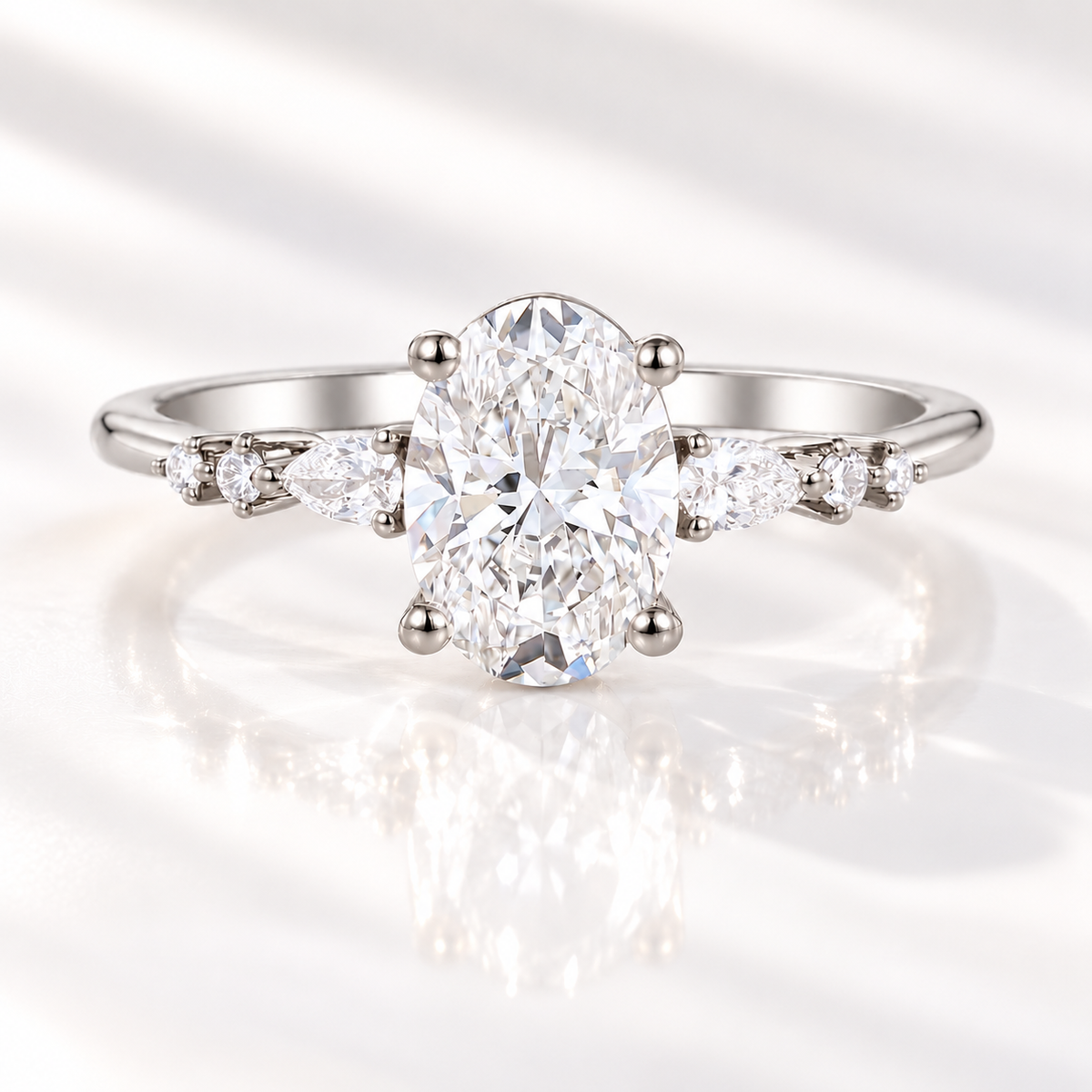 Oval cut diamond center stone in a four-prong white gold setting, flanked by a pear cut and two round side stones on each side of the band