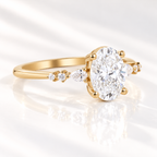Angled view of an oval cut diamond center stone in a four-prong yellow gold setting with pear cut and round side stones along the band