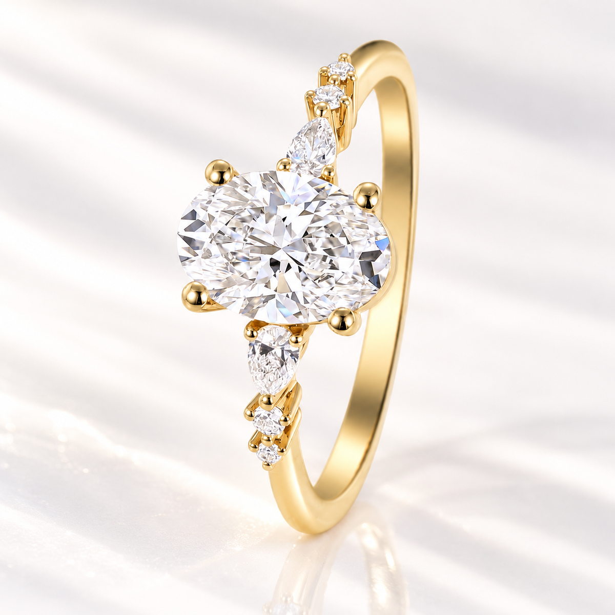 Oval cut diamond center stone in a four-prong yellow gold setting with pear cut and round side stones graduating down the slim band