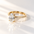 Angled view of an oval cut diamond center stone in a four-prong yellow gold setting with round diamonds set along the band