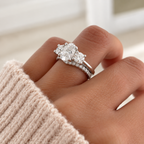 Oval cut diamond center stone in a prong white gold setting, flanked by a round side stone on each side, stacked with a pavé diamond band