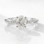 A high-quality, close-up product photograph of the same delicate engagement ring design, now in high-polish silver. It features the central oval-cut solitaire diamond held by four prongs, on a white reflective surface with soft lighting.