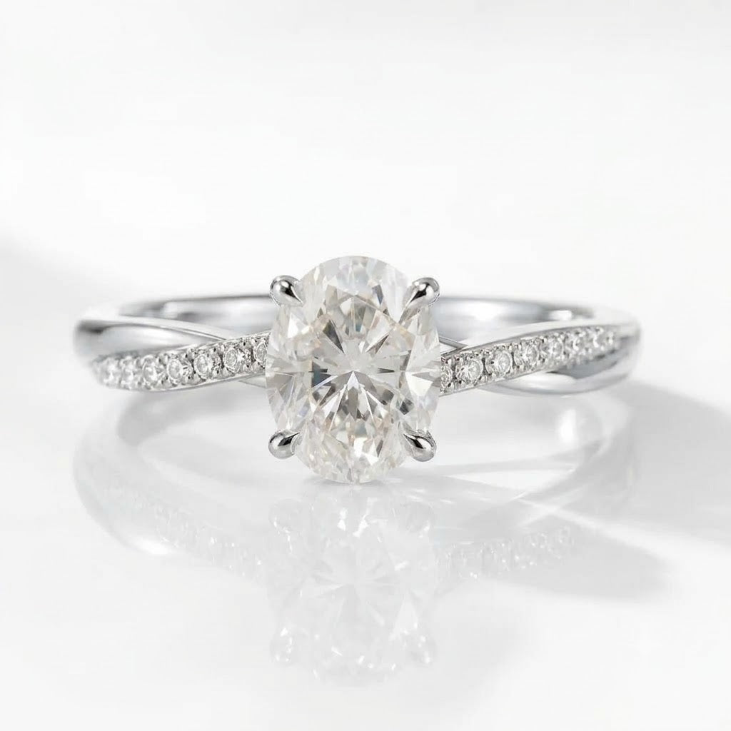 A high-quality, close-up product photograph of the same delicate engagement ring design, now in high-polish silver. It features the central oval-cut solitaire diamond held by four prongs, on a white reflective surface with soft lighting.