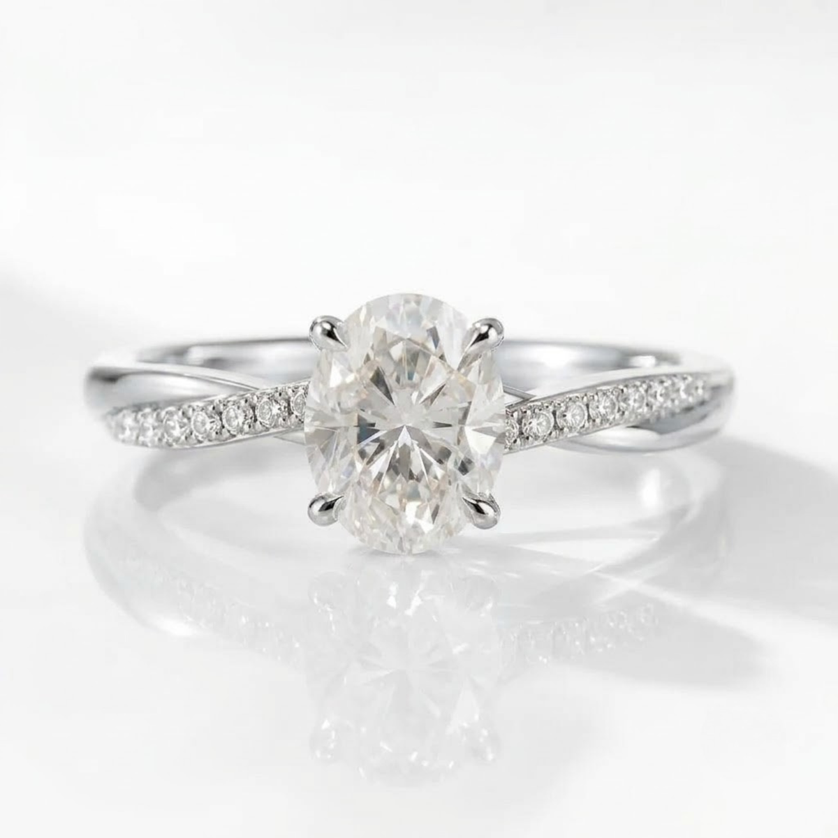 A high-quality, close-up product photograph of the same delicate engagement ring design, now in high-polish silver. It features the central oval-cut solitaire diamond held by four prongs, on a white reflective surface with soft lighting.