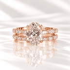 Oval diamond engagement ring with a hidden halo and a matching pavé wedding band, set in rose gold on a glossy white surface.