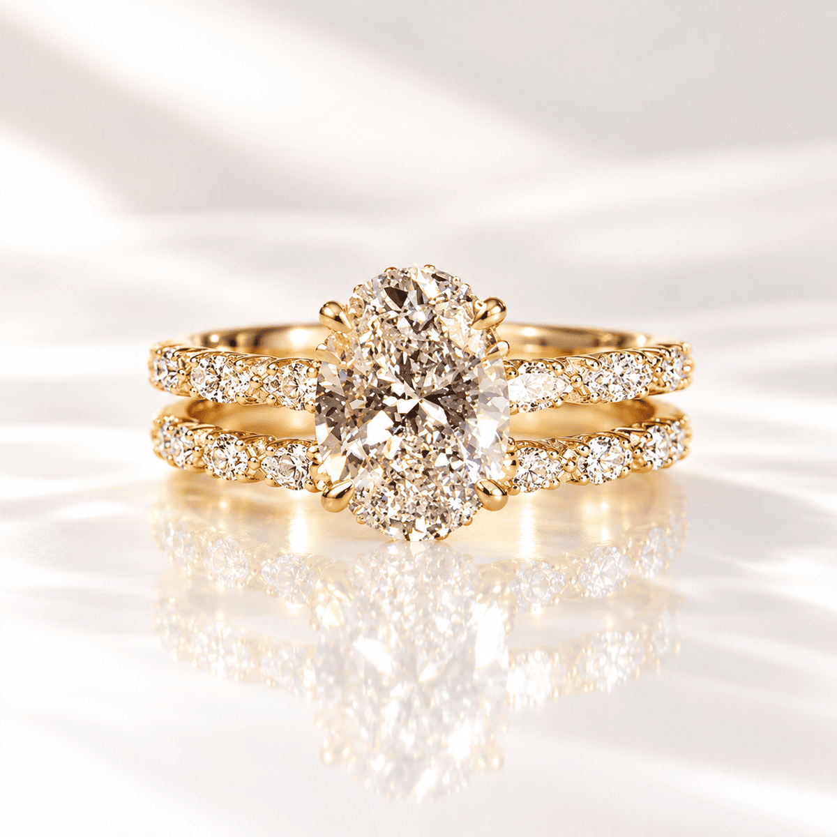 Oval diamond engagement ring with a hidden halo and a matching pavé wedding band, set in yellow gold on a reflective white surface.