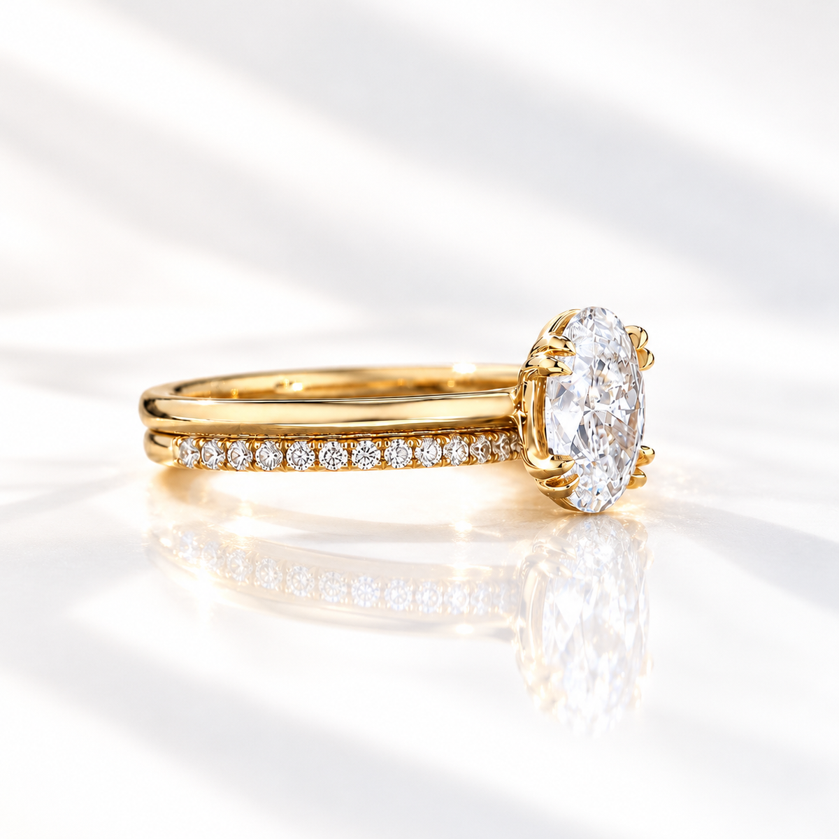 Side profile of a yellow gold oval diamond engagement ring with double prongs stacked with a slim pavé wedding band, showing the thin band and small round diamonds