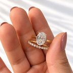 Open hand with mauve nails holding a yellow gold oval diamond solitaire engagement ring beside a slim wedding band set with round diamonds