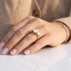 Three-stone oval cut diamond engagement ring with pear-shaped side stones set in yellow gold, worn on a hand.