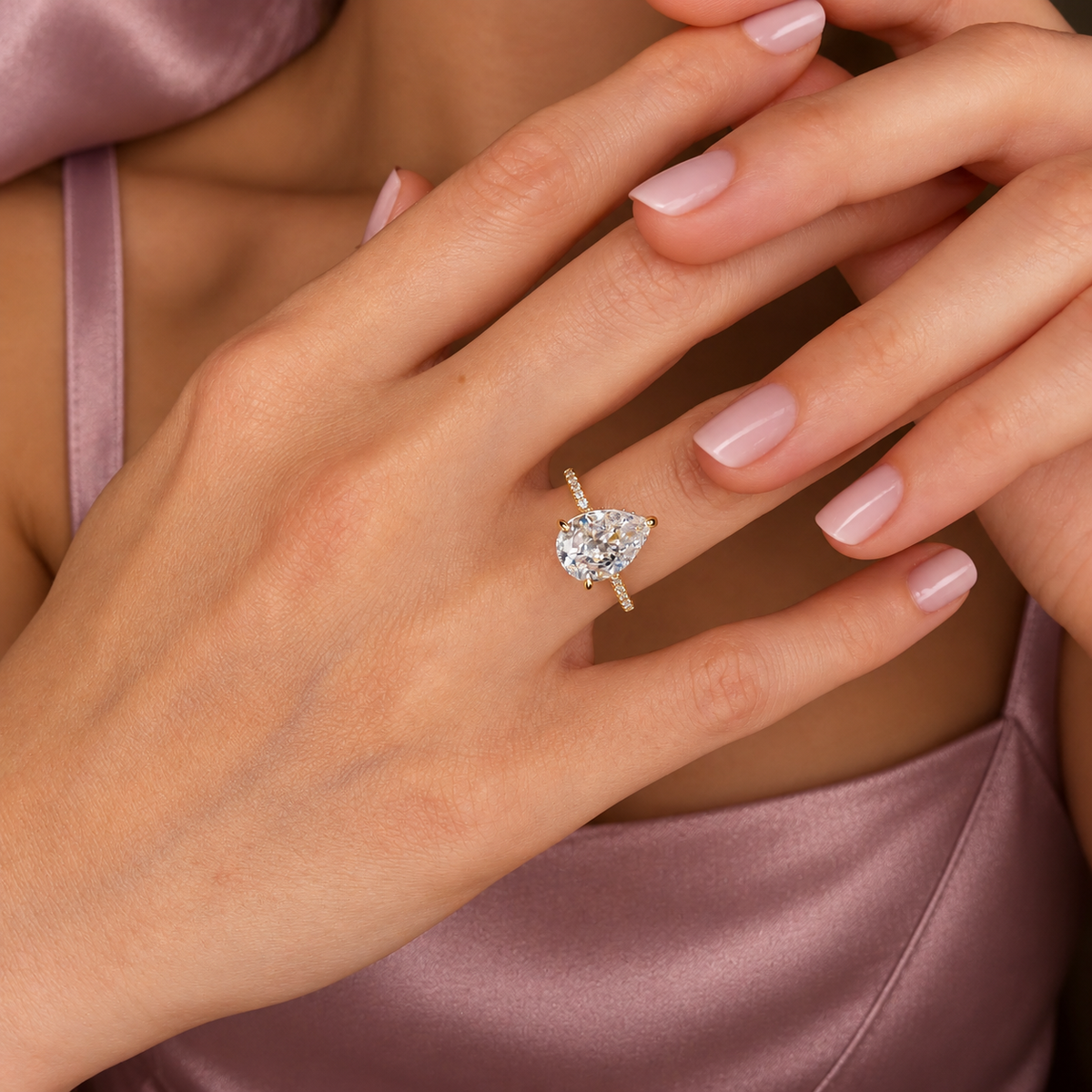 Pear cut diamond center stone in a prong yellow gold setting with a pavé diamond band viewed from the side