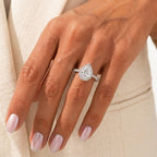 Pear cut halo diamond engagement ring set in white gold or platinum with a sparkling pavé diamond band, worn on a hand.