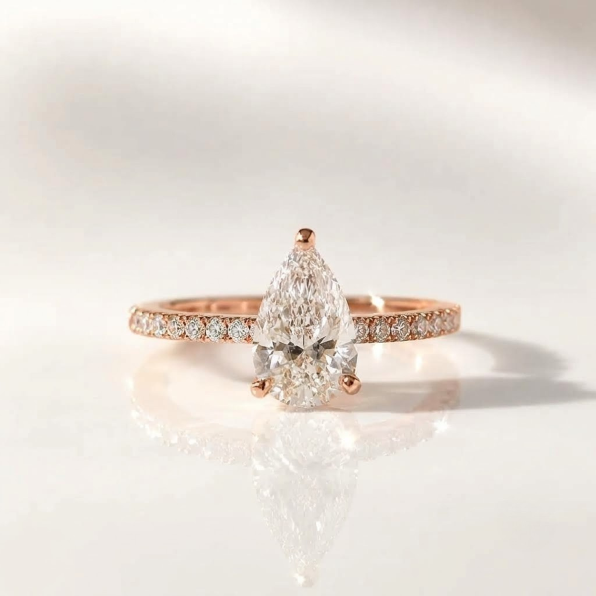 Pear-shaped diamond ring with pavé band in rose gold.