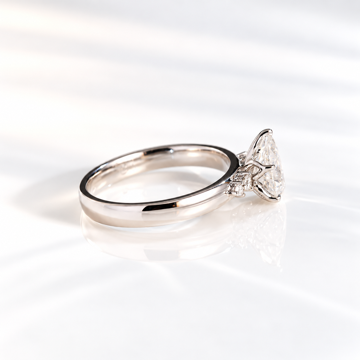 Angled view of a pear solitaire engagement ring with a pear cut diamond in a five-prong white gold setting and round side stones on a thick polished band