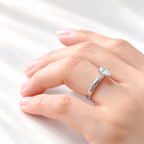 Side view of a pear solitaire engagement ring with a pear cut diamond in a prong white gold setting and round side stones on a thick band