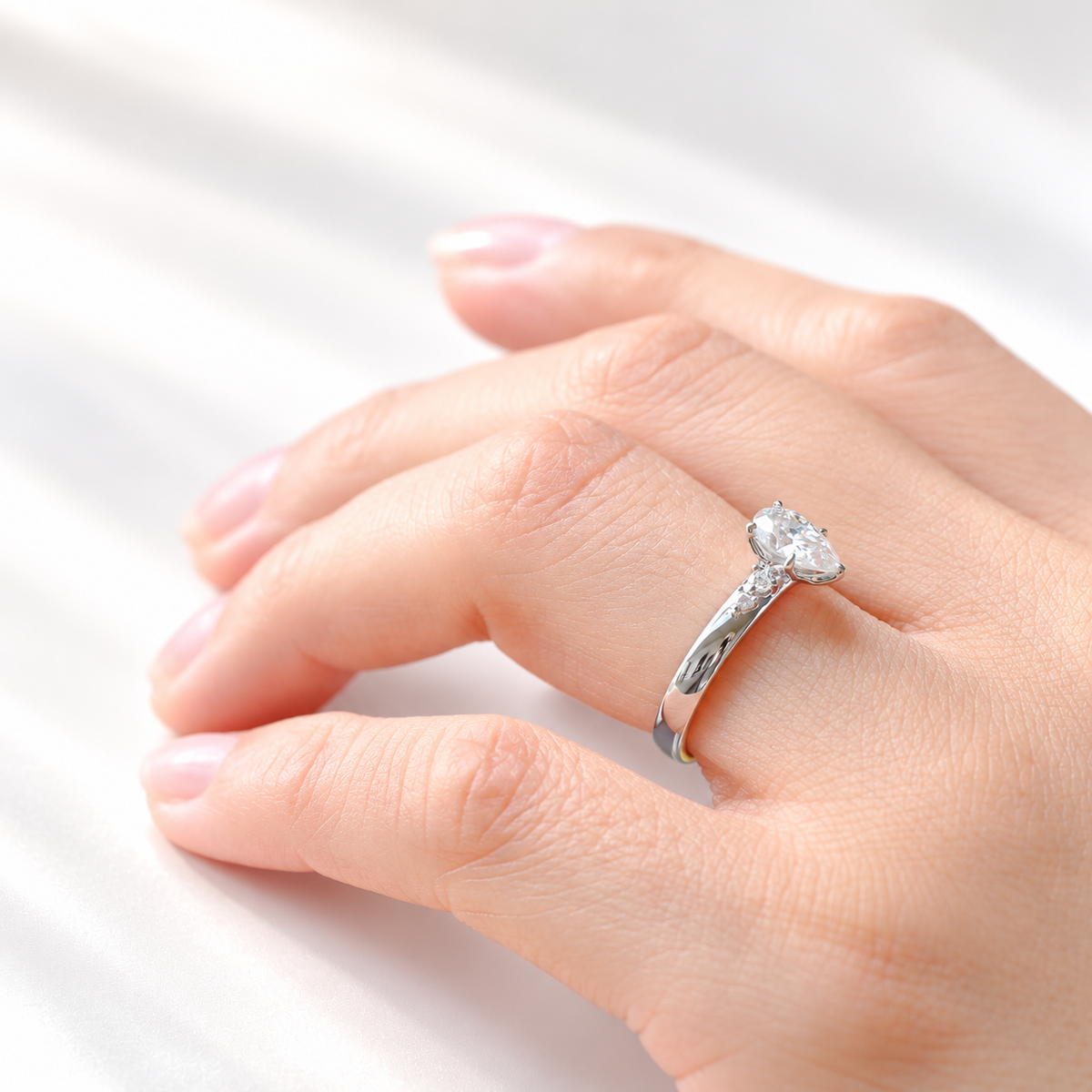 Side view of a pear solitaire engagement ring with a pear cut diamond in a prong white gold setting and round side stones on a thick band