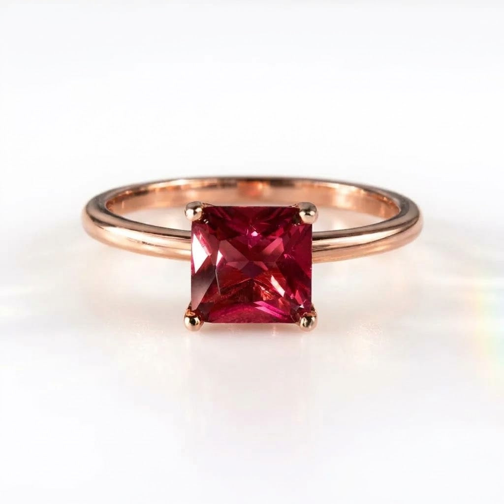 A square-cut pink gemstone ring set in a rose gold band, photographed on a clean white background.