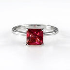 A silver band ring featuring a square-cut, vibrant red gemstone in a four-prong setting, photographed on a clean white background.