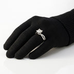 Princess cut diamond solitaire engagement ring set in white gold or platinum with a twisted, bypass pavé diamond band, displayed on a black-gloved hand.