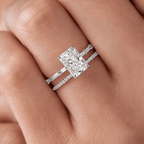 Close-up of a hand wearing a white gold radiant cut diamond engagement ring with baguette accents, stacked with a thin pavé diamond wedding band.