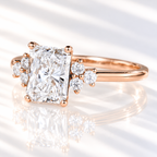 Radiant cut diamond center stone in a four-prong rose gold setting with clusters of three round side stones on a slim polished band