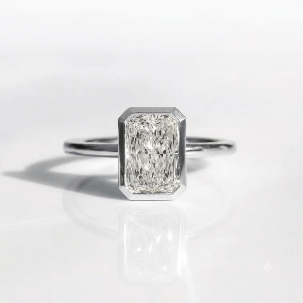 An emerald-cut diamond ring in a silver-toned setting on a clean white reflective surface.